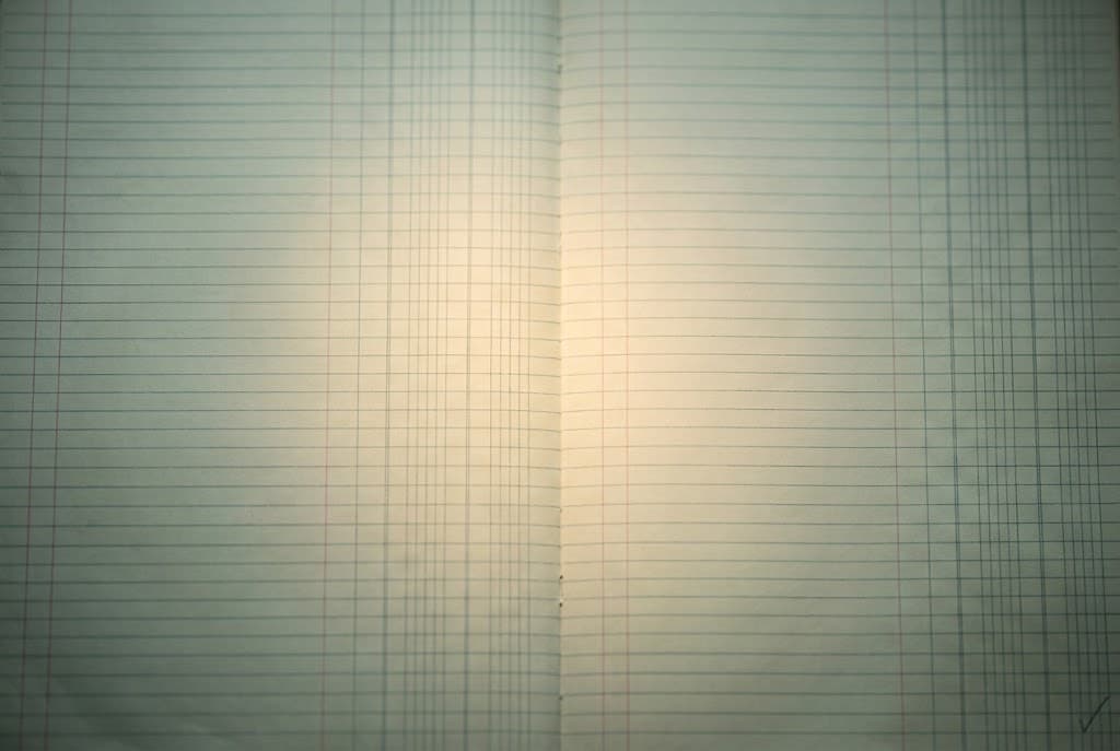 An empty pale-green ledger pad under a pool of warm light, one tick mark in the corner